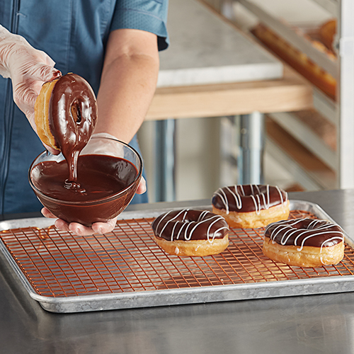 Donuts covered in chocolate icing and someone dipping plain donuts in a bowl of icing